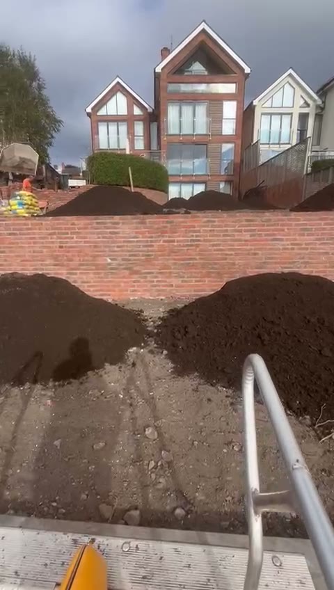 Garden reduced to formation with topsoil heaped behind the brick wall