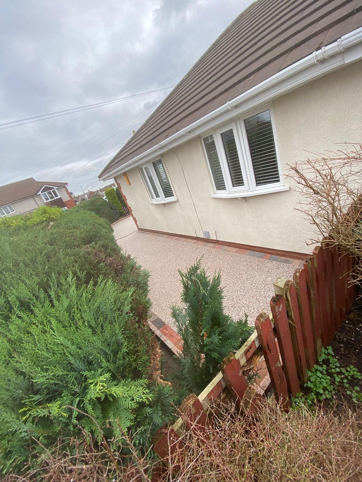 Finished light buff resin driveway with a curved edge to the hedge line